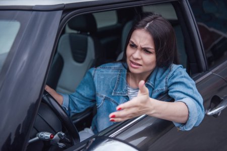Photo for Beautiful girl in jean jacket is looking ahead with irritation while driving a car - Royalty Free Image