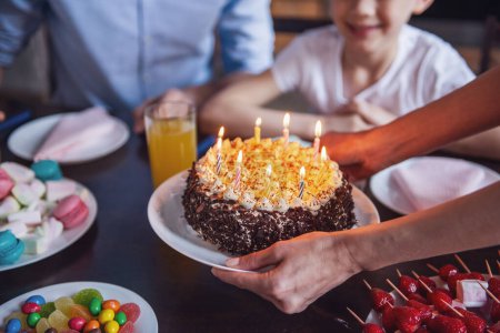 Foto de Familia celebrando cumpleaños. Imagen recortada de mamá sosteniendo un pastel de cumpleaños con velas - Imagen libre de derechos