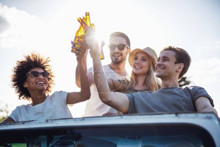 Téléchargez les photos : Heureux les jeunes gens sont des bouteilles de boissons et souriant tout en voyageant en voiture par temps ensoleillé - en image libre de droit