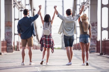 Foto de Vista posterior de jóvenes alegres sosteniendo y levantando las manos mientras caminan por la ciudad - Imagen libre de derechos