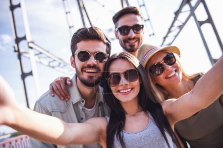 Photo for Cheerful young people are doing selfie, looking at camera and smiling while walking outdoors - Royalty Free Image