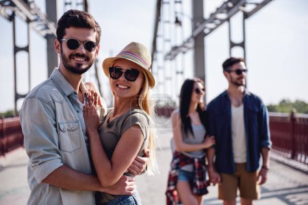 Téléchargez les photos : Jeunes couples joyeux sont câlins, regardant la caméra et souriant tout en marchant à l'extérieur - en image libre de droit