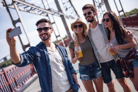 Téléchargez les photos : Jeunes gens joyeux font selfie en utilisant un téléphone intelligent et souriant tout en marchant à l'extérieur - en image libre de droit