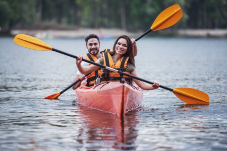Foto de Feliz joven pareja en chalecos de mar está sonriendo mientras navega un kayak - Imagen libre de derechos