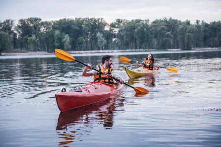 Photo for Happy young couple in sea vests is smiling while sailing kayaks - Royalty Free Image
