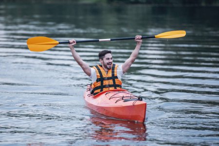 Téléchargez les photos : Beau jeune homme en gilet de mer sourit tout en naviguant en kayak - en image libre de droit