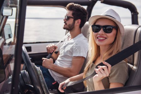 Téléchargez les photos : Beau jeune couple attache les ceintures de sécurité et sourit tout en voyageant en voiture - en image libre de droit