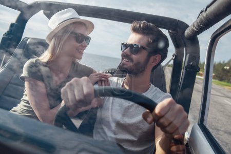 Téléchargez les photos : Beau jeune couple parle et sourit tout en voyageant en voiture par temps ensoleillé - en image libre de droit