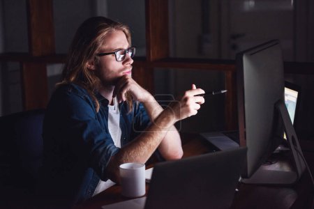 Téléchargez les photos : Beau jeune homme d'affaires aux cheveux blonds longueur épaule et en tenue décontractée et lunettes travaille avec un ordinateur la nuit - en image libre de droit