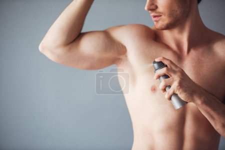 Photo for Cropped image of handsome young man with bare torso using a spray deodorant, on gray background - Royalty Free Image