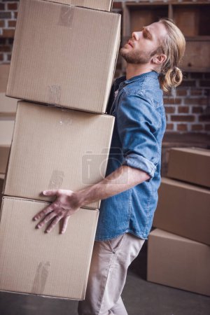 Téléchargez les photos : Beau gars porte des boîtes en carton tout en déménageant dans un nouvel appartement - en image libre de droit