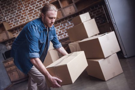 Photo for Handsome guy is lifting a cardboard box while moving into new apartment - Royalty Free Image