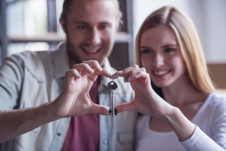 Photo for Beautiful young couple is holding a key, making a heart and smiling while moving into new apartment - Royalty Free Image