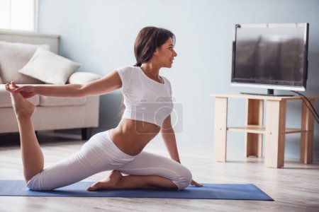 Foto de Hermosa chica deportiva está sonriendo mientras hace yoga en casa - Imagen libre de derechos