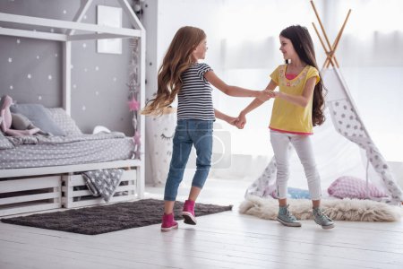 Téléchargez les photos : Deux petites filles heureuses dansent et sourient tout en jouant dans la chambre des enfants à la maison - en image libre de droit