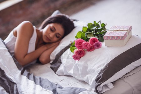 Téléchargez les photos : Belle fille dort au lit à la maison, des fleurs et une boîte cadeau couché sur oreiller près - en image libre de droit