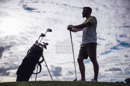 Téléchargez les photos : Portrait complet d'un beau gars tenant un club de golf et regardant loin tout en se tenant sur le terrain de golf - en image libre de droit