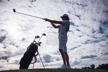 Retrato de cuerpo entero del hombre guapo eligiendo un club de golf mientras está parado en el campo de golf

