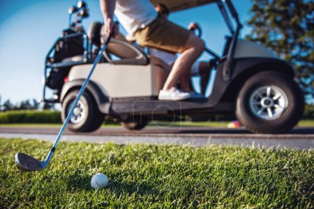 Téléchargez les photos : Image recadrée de beaux hommes conduisant une voiturette de golf, un gars soulève un club de golf à la balle, balle en bref - en image libre de droit
