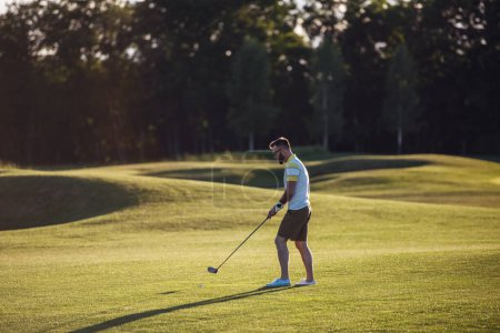 Foto de Retrato de cuerpo entero del chico guapo usando un club de golf mientras juega al golf - Imagen libre de derechos