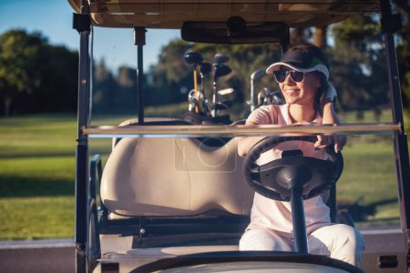 Téléchargez les photos : Belle jeune femme sourit tout en conduisant une voiturette de golf - en image libre de droit