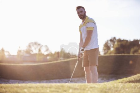 Foto de Chico guapo está usando un club de golf mientras juega al golf, hermoso sol brillando - Imagen libre de derechos