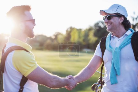 Foto de Hombres guapos se dan la mano y sonríen cuando se reúnen en un campo de golf - Imagen libre de derechos