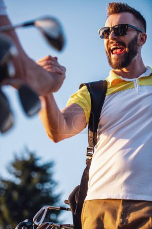 Téléchargez les photos : Les beaux hommes serrent la main et sourient quand ils se rencontrent sur un terrain de golf - en image libre de droit
