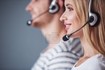 Photo for Side view of beautiful young couple in headsets looking forward and smiling, on gray background - Royalty Free Image