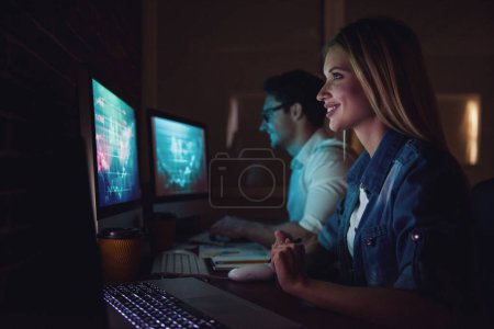 Téléchargez les photos : Beau jeune homme d'affaires et femme travaillent avec ordinateur au bureau la nuit - en image libre de droit