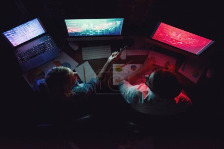 Téléchargez les photos : Vue de dessus de beau jeune homme d'affaires et femme travaillant avec ordinateur dans le bureau la nuit - en image libre de droit