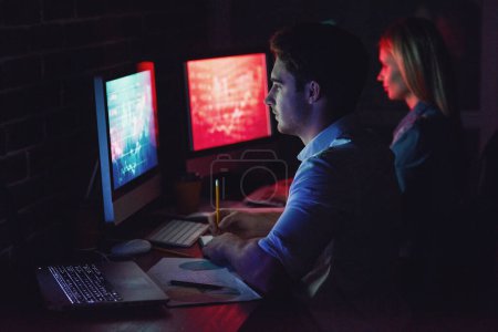 Téléchargez les photos : Beau jeune homme d'affaires et femme travaillent avec ordinateur au bureau la nuit - en image libre de droit