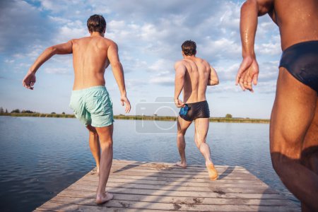 Photo for Handsome guys are jumping from pier into the lake, beautiful view - Royalty Free Image