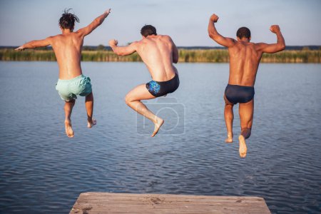 Foto de Chicos guapos están saltando desde el muelle en el lago, hermosa vista - Imagen libre de derechos