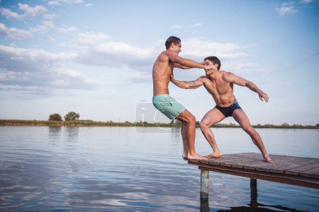 Photo for Handsome guys are pushing each other from pier into the lake, beautiful view - Royalty Free Image