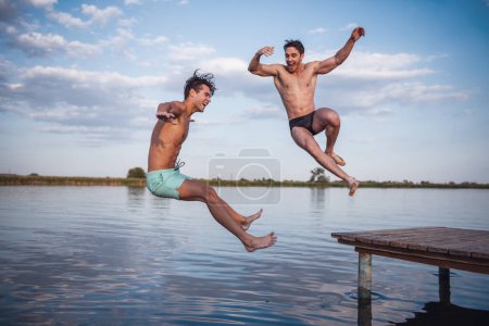 Téléchargez les photos : Beaux gars sautent de la jetée dans le lac, belle vue - en image libre de droit