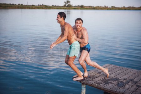 Téléchargez les photos : Beaux gars se poussent mutuellement de la jetée dans le lac, belle vue - en image libre de droit