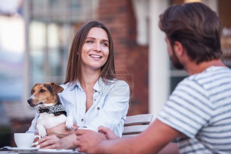 Téléchargez les photos : Belle femme tient son chien mignon, buvant du café et souriant tout en parlant avec l'homme au café - en image libre de droit