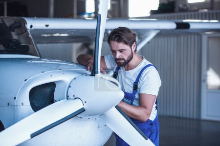 Photo for Handsome bearded mechanic in uniform is examining an aircraft in hangar - Royalty Free Image