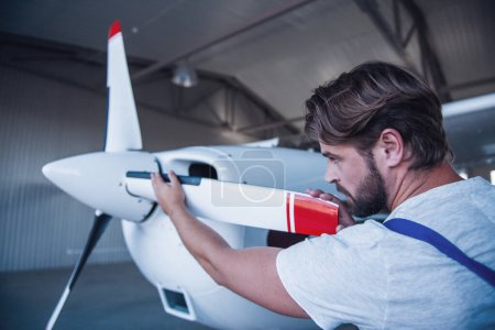 Foto de Guapo barbudo mecánico de uniforme está examinando un avión en el hangar - Imagen libre de derechos
