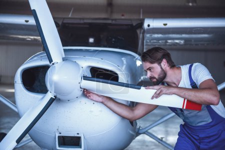 Foto de Guapo barbudo mecánico de uniforme está examinando un avión en el hangar - Imagen libre de derechos
