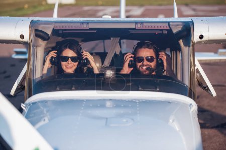 Foto de Hermosa pareja en auriculares de aviación está mirando a la cámara y sonriendo mientras está sentado en aviones listos para volar - Imagen libre de derechos