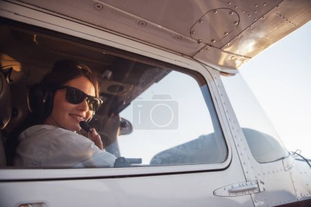Foto de Hermosa mujer en auriculares de aviación está mirando a la cámara y sonriendo mientras está sentado en aviones listos para volar - Imagen libre de derechos