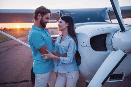 Foto de Hermosa pareja romántica está abrazando y sonriendo mientras está de pie en tierra de despegue cerca del avión - Imagen libre de derechos