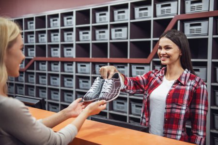 Téléchargez les photos : Belle fille offre une paire de chaussures de bowling au client et souriant - en image libre de droit