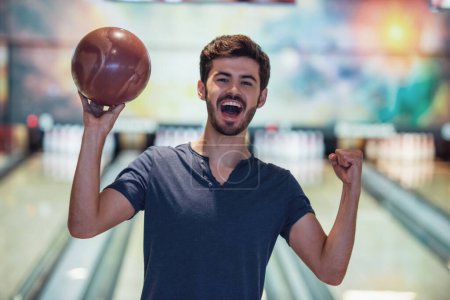 Téléchargez les photos : Un beau mec tient une boule de bowling, regarde la caméra et sourit prêt à jouer au bowling - en image libre de droit