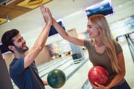 Photo for Beautiful girl and handsome guy are holding bowling balls, giving high five and smiling ready to play - Royalty Free Image