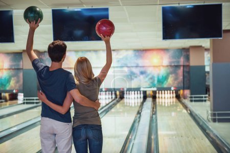 Téléchargez les photos : Vue arrière de la belle fille et beau gars tenant des boules de bowling et câlins tout en jouant - en image libre de droit