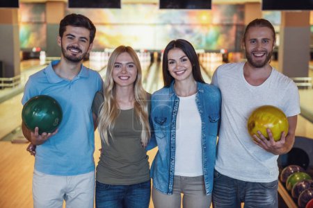 Téléchargez les photos : De jeunes amis heureux tiennent des couilles, regardent la caméra et sourient tout en jouant au bowling ensemble - en image libre de droit