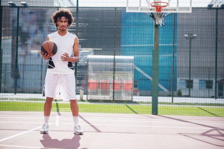 Photo for Full length of attractive basketball player holding a ball while playing on basketball court outdoors - Royalty Free Image